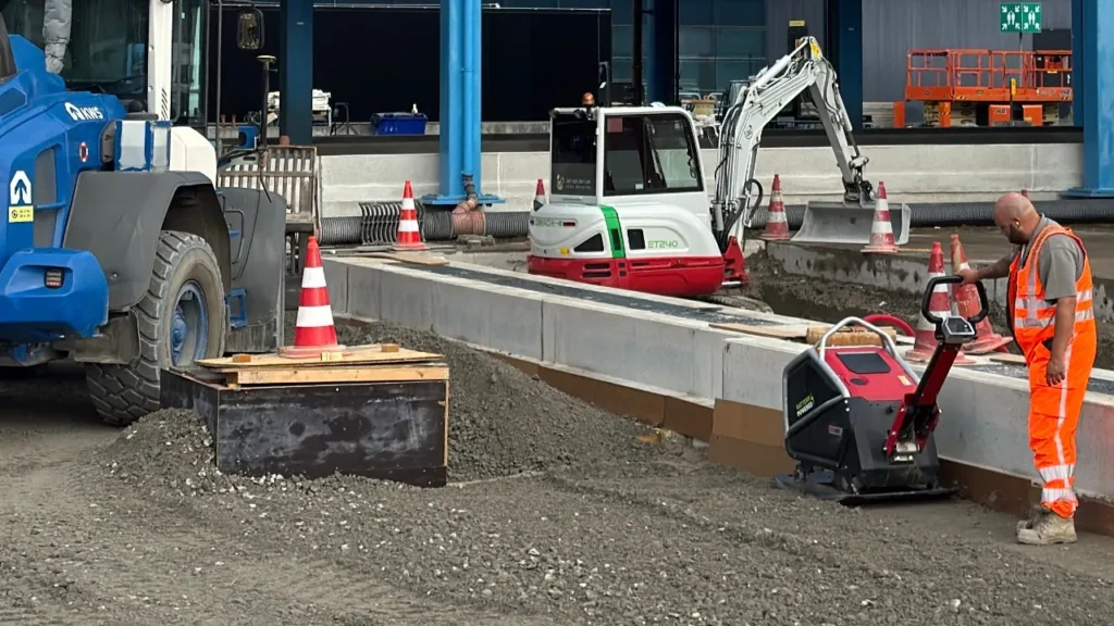 moderne elektrische trilplaat op bouwplaats naast accu’s en twee uitvoerders met tablet