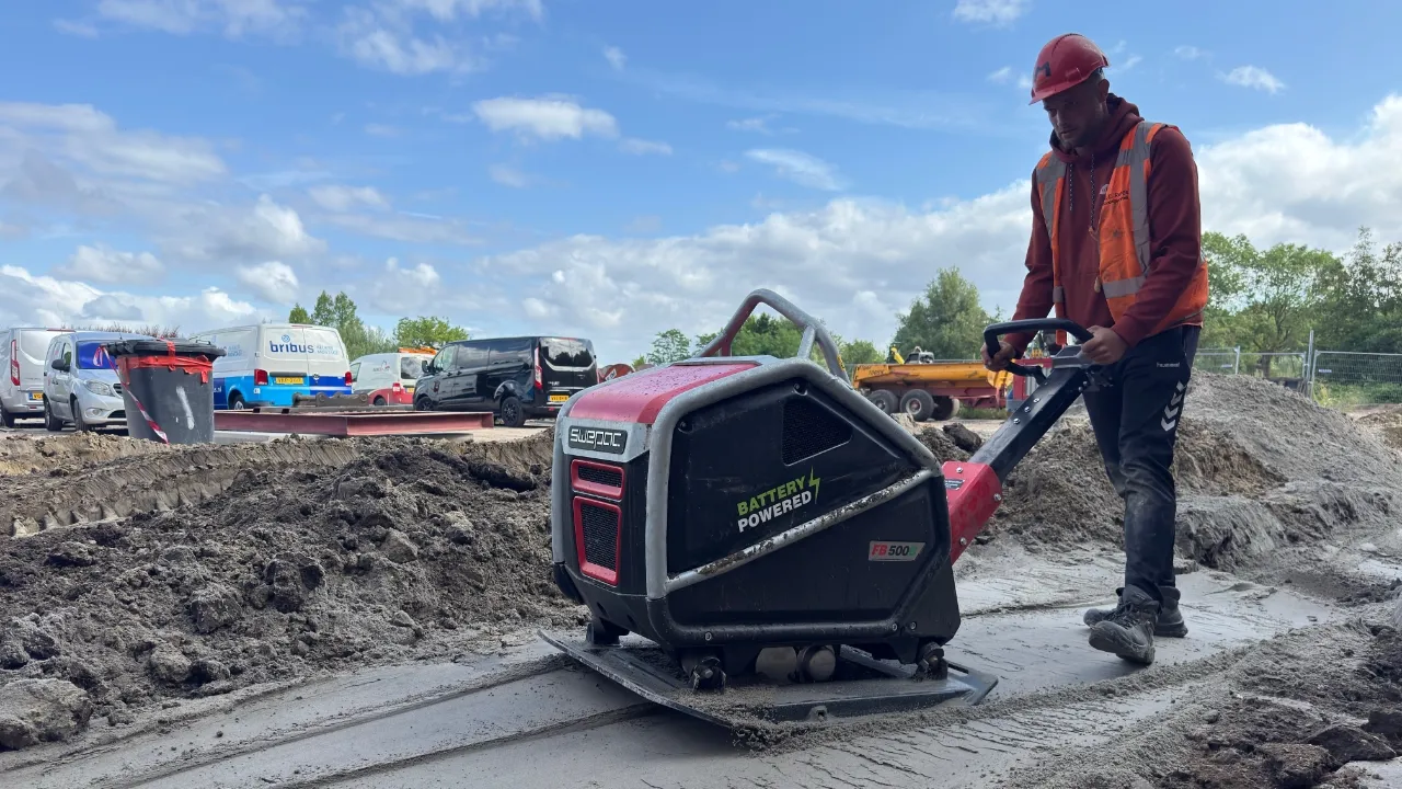 stratenmaker bedient een compacte accu trilplaat op straatzand in een rustige binnenstad