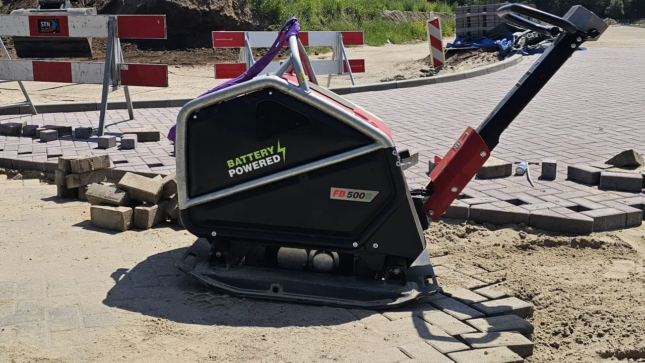 stratenmaker gebruikt een accu trilplaat in een smalle woonstraat tussen geparkeerde auto’s en rijtjeshuizen