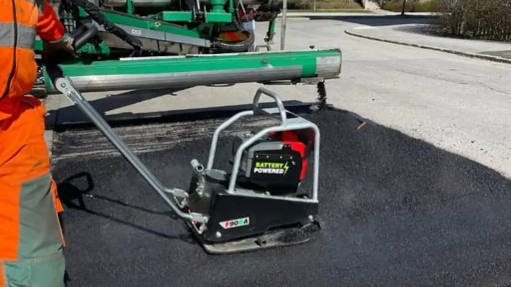 straatwerker gebruikt een accu trilstamper in een smalle binnenstedelijke straat met zero-emissieborden