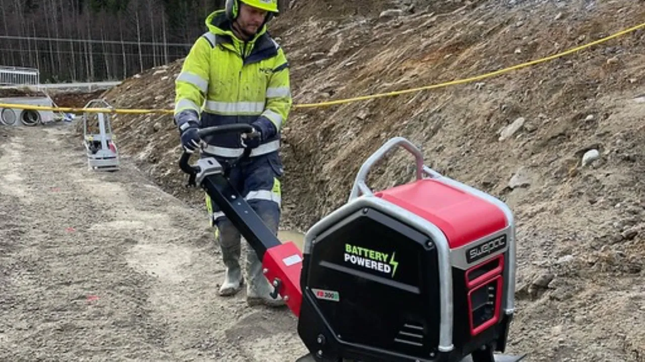 bouwvakker gebruikt een accu trilstamper in een smalle sleuf langs een stoep in een woonwijk