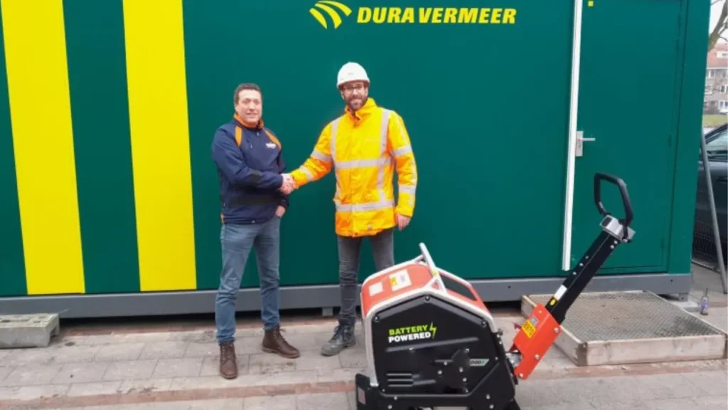 bouwplaats in de stad waar een medewerker een elektrische trilplaat aansluit op een mobiele batterijunit