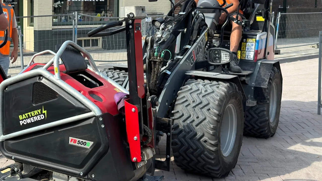 professionele accu trilplaat verdicht zandbaan naast trottoir, met meetsonde voor controle van verdichtingskwaliteit