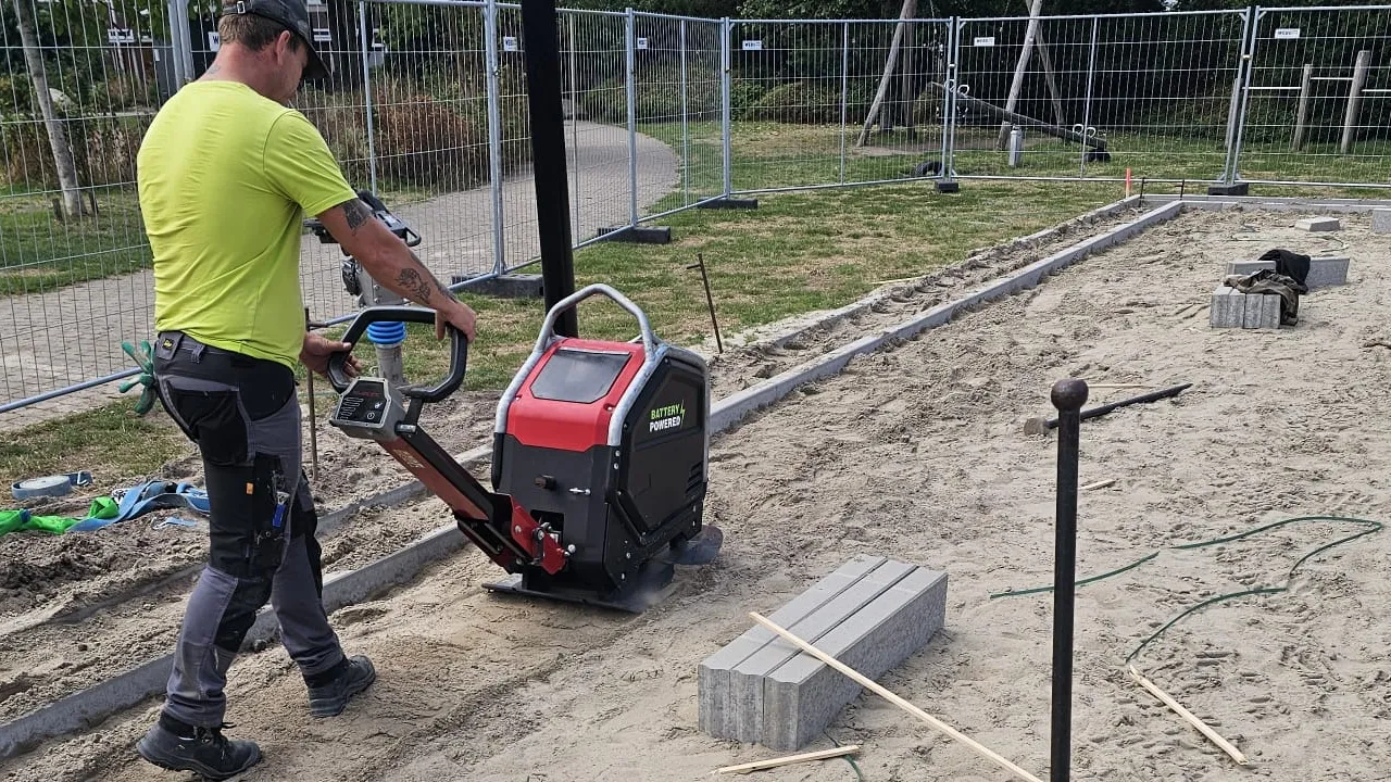 zware accu trilplaat verdicht zandbed op gww-bouwplaats bij schemering, accupack duidelijk zichtbaar