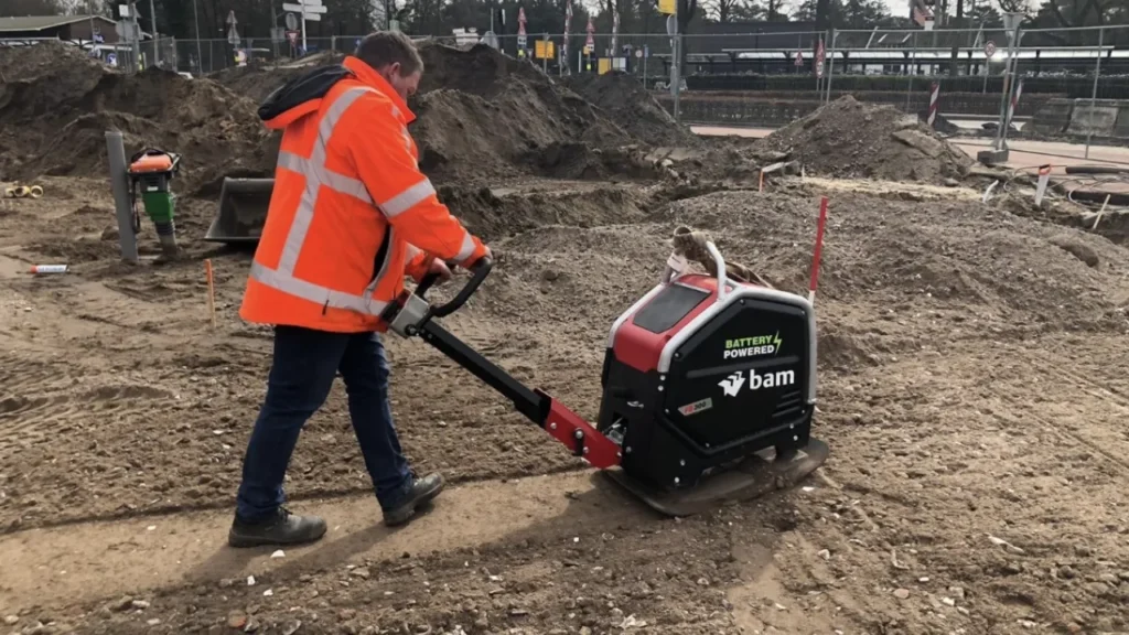 stratenmaker bedient zware accu trilplaat naast grotere trilplaat op gww-werkterrein bij schemerlicht